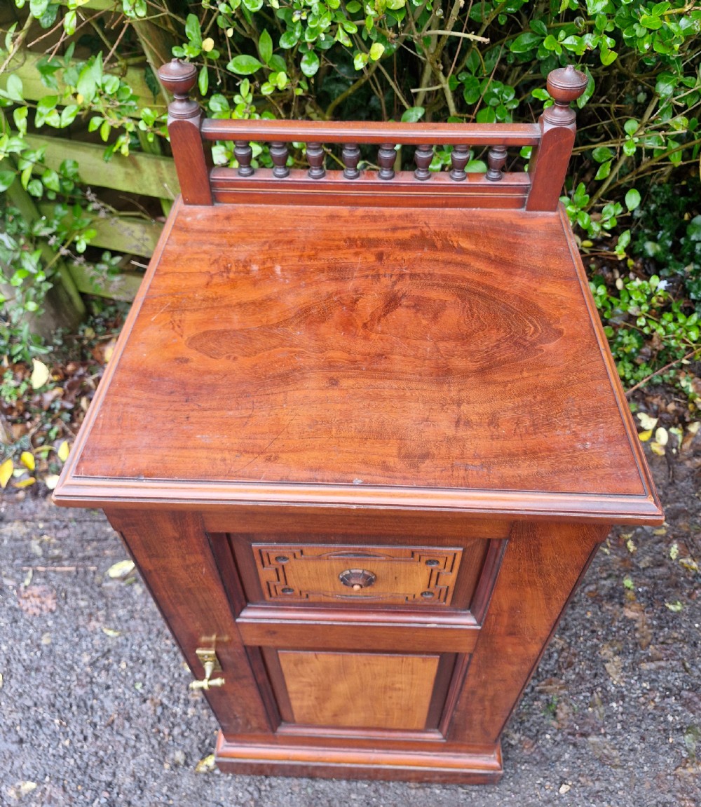 A late Victorian mahogany bedside cabinet featuring a spindle gallery top, a carved fielded door panel, and a brass latch. View VI