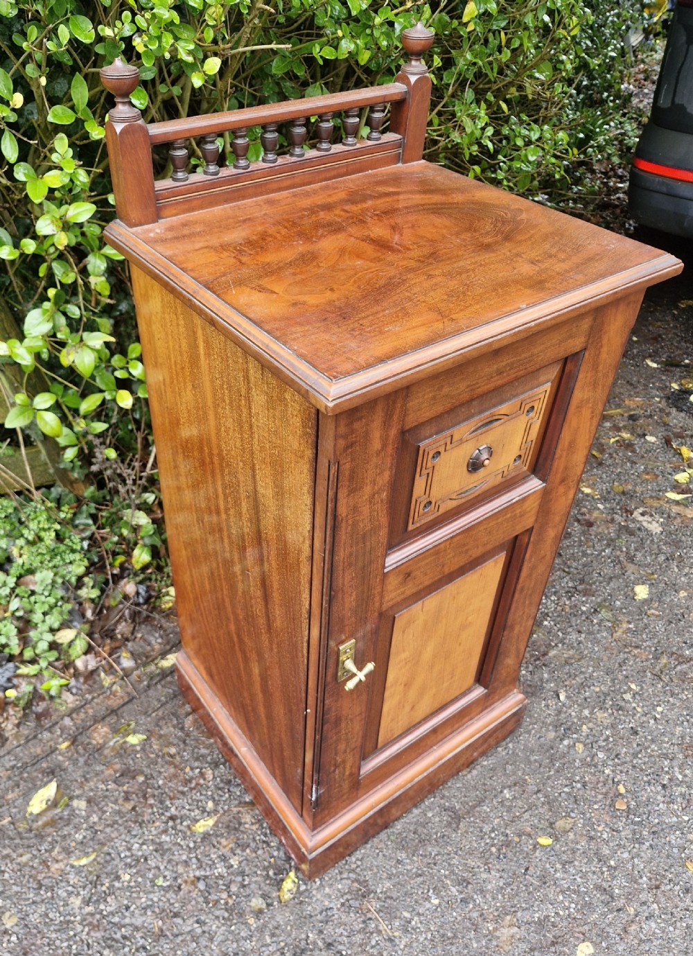 A late Victorian mahogany bedside cabinet featuring a spindle gallery top, a carved fielded door panel, and a brass latch. View VII