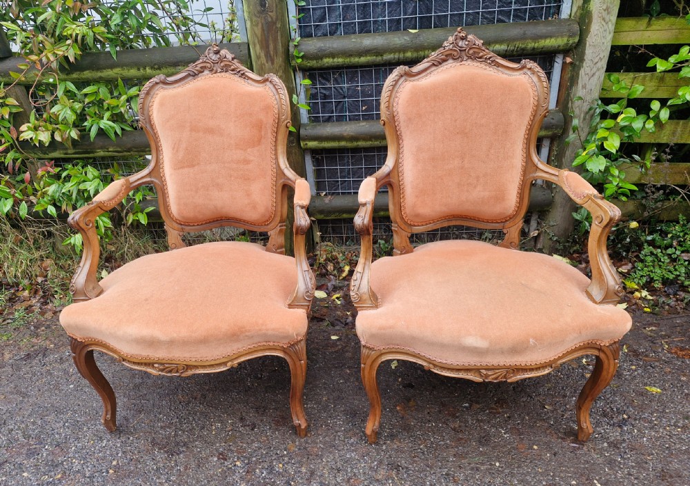 A pair of French Louis XV style carved walnut fauteuil armchairs with open padded armrests and peach velvet upholstery.
