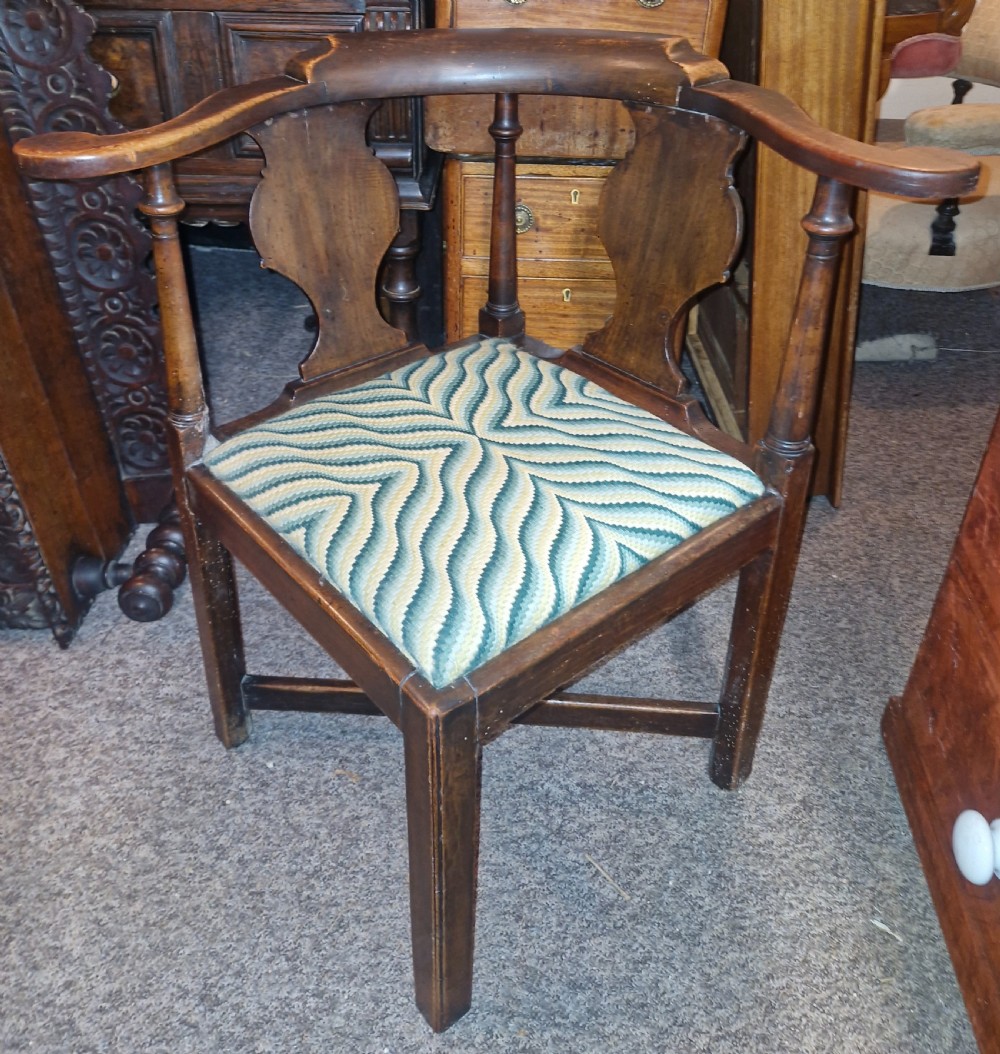 A late Georgian dark walnut corner chair featuring a curved continuous armrest, shaped splats, turned supports, and a green flame-stitch pattern drop-in seat.