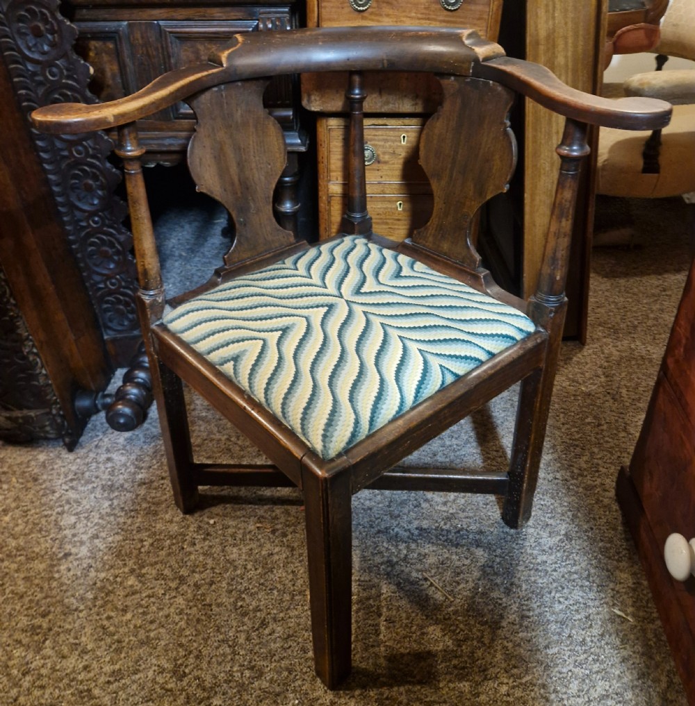 A late Georgian dark walnut corner chair featuring a curved continuous armrest, shaped splats, turned supports, and a green flame-stitch pattern drop-in seat. View II