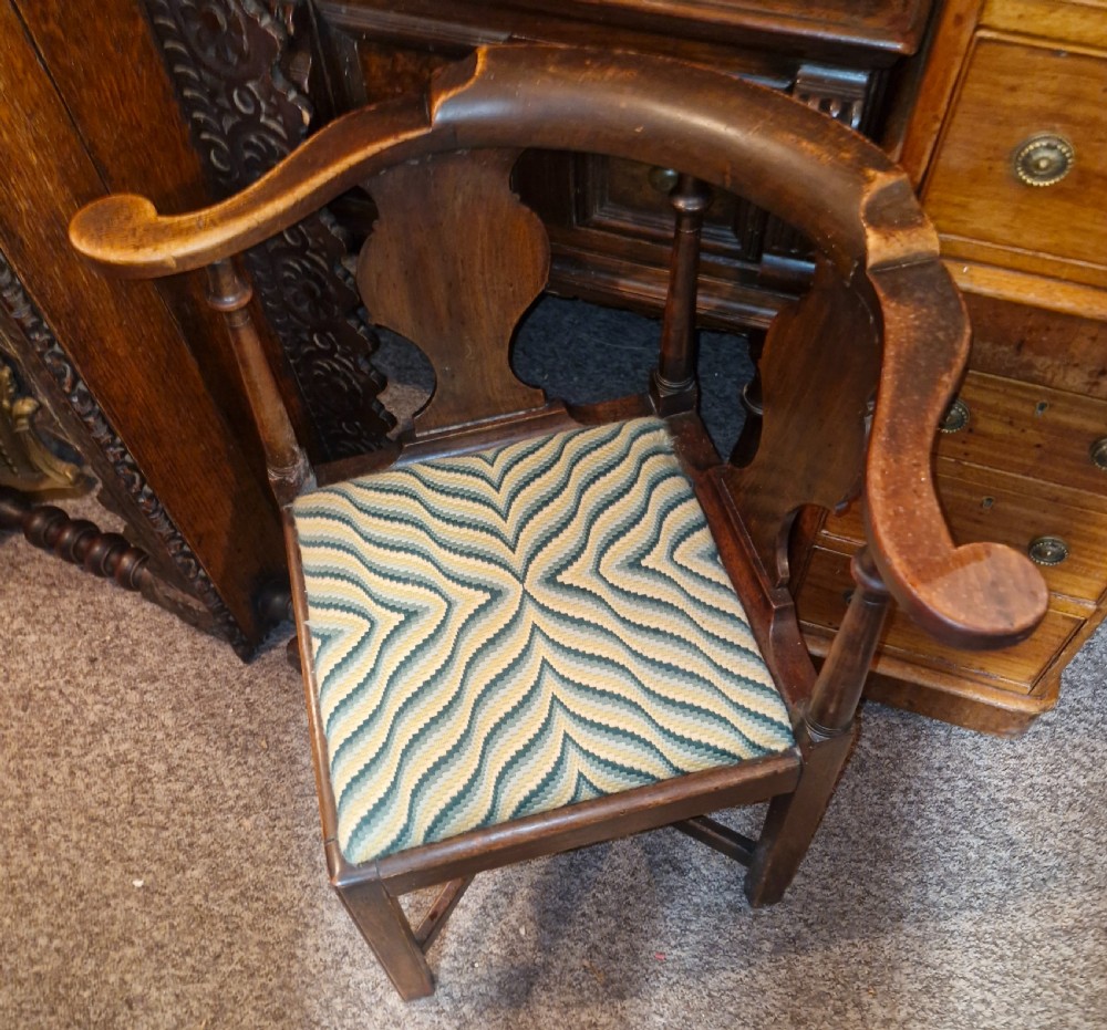 A late Georgian dark walnut corner chair featuring a curved continuous armrest, shaped splats, turned supports, and a green flame-stitch pattern drop-in seat. View III