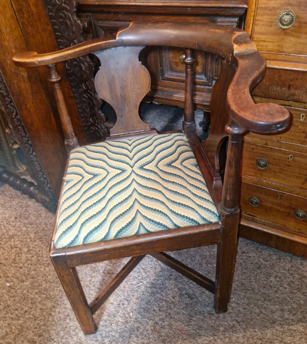 A late Georgian dark walnut corner chair featuring a curved continuous armrest, shaped splats, turned supports, and a green flame-stitch pattern drop-in seat. View IV