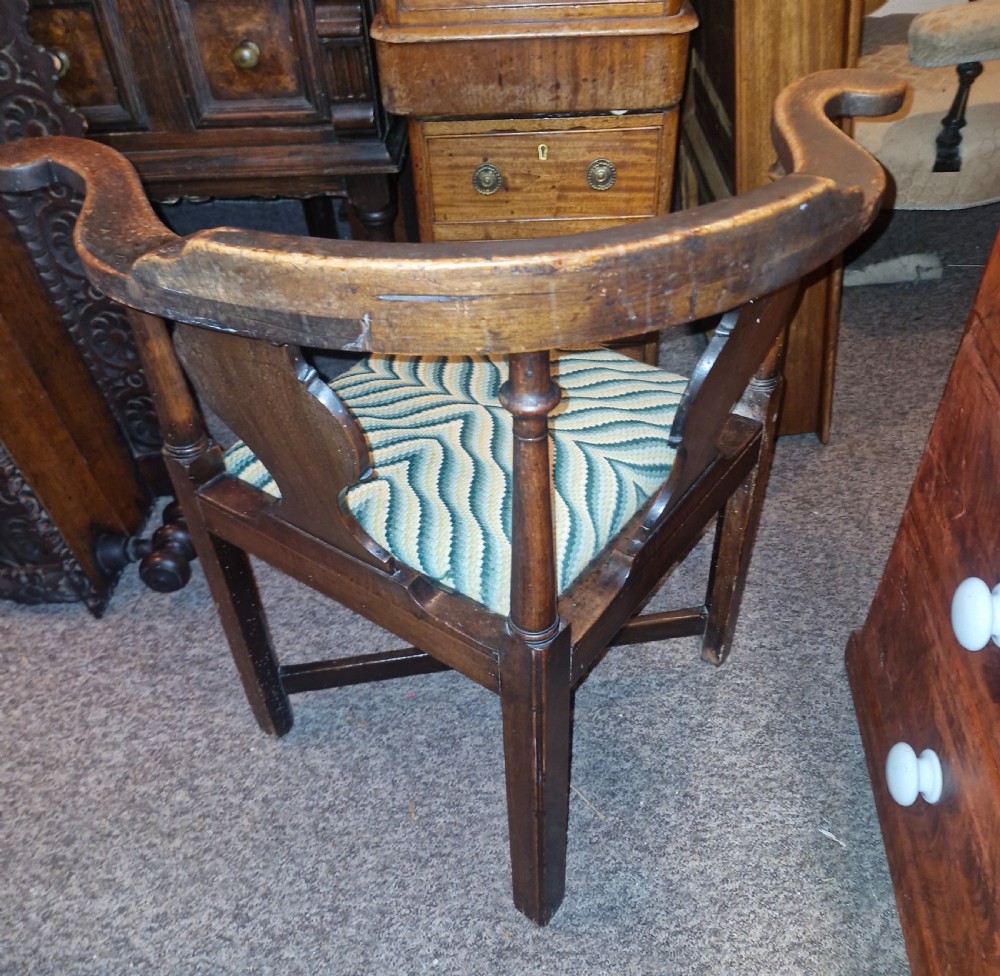 A late Georgian dark walnut corner chair featuring a curved continuous armrest, shaped splats, turned supports, and a green flame-stitch pattern drop-in seat. View VI