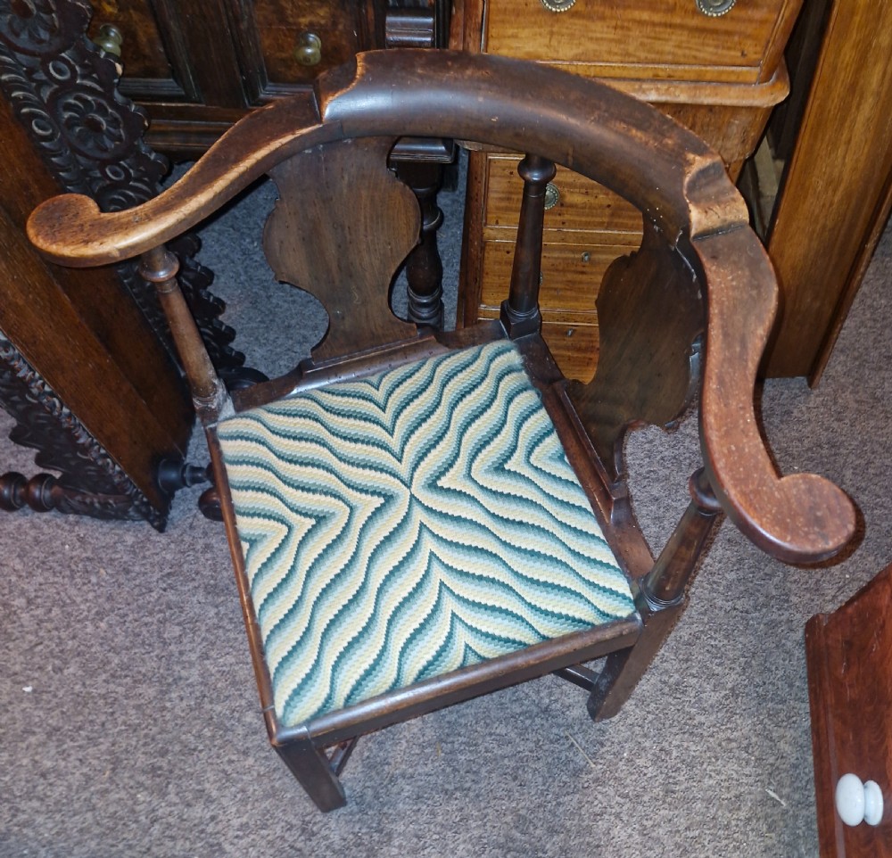 A late Georgian dark walnut corner chair featuring a curved continuous armrest, shaped splats, turned supports, and a green flame-stitch pattern drop-in seat. View VII