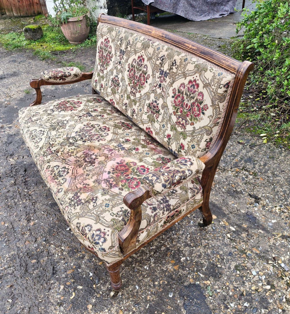 A late Victorian rosewood settee featuring delicate marquetry inlay, patterned upholstery, padded armrests, and turned legs on brass castors. View II