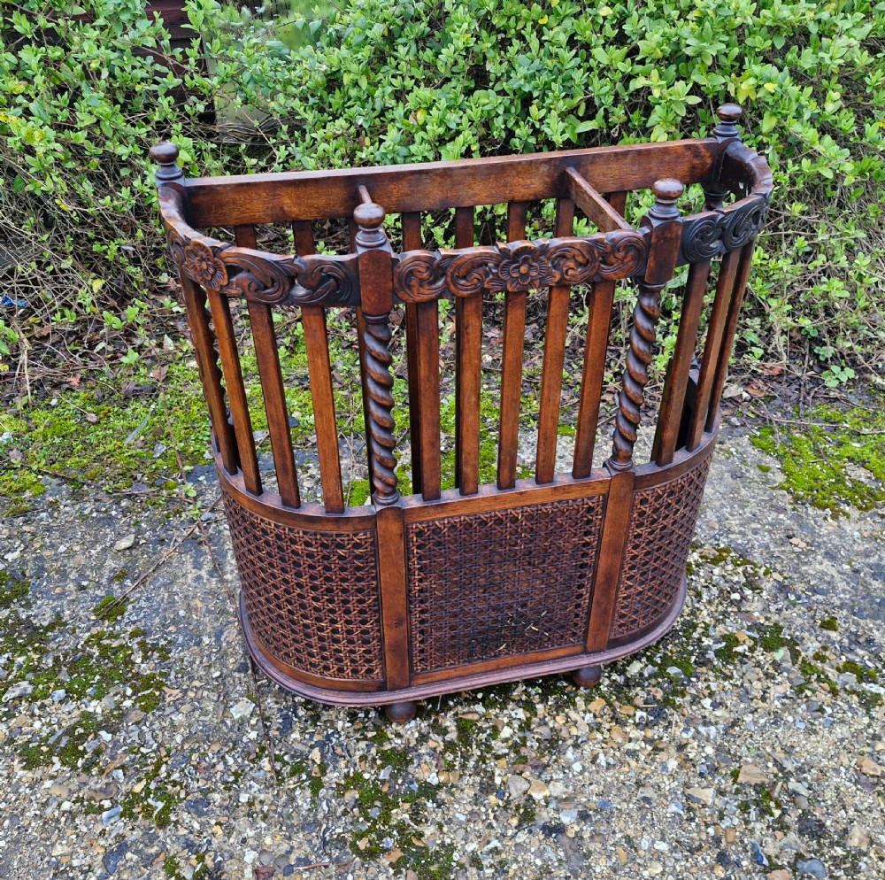 A carved dark oak stick and umbrella stand featuring barley twist supports, vertical wooden slats, and lower woven cane panels.