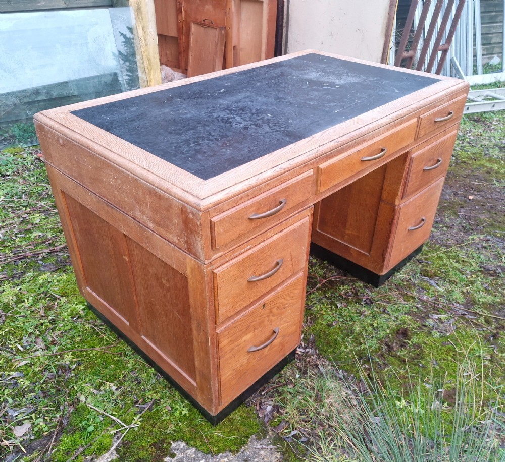 An Art Deco oak pedestal office desk featuring a dark inset writing top, streamlined drawers, and metal pull handles.