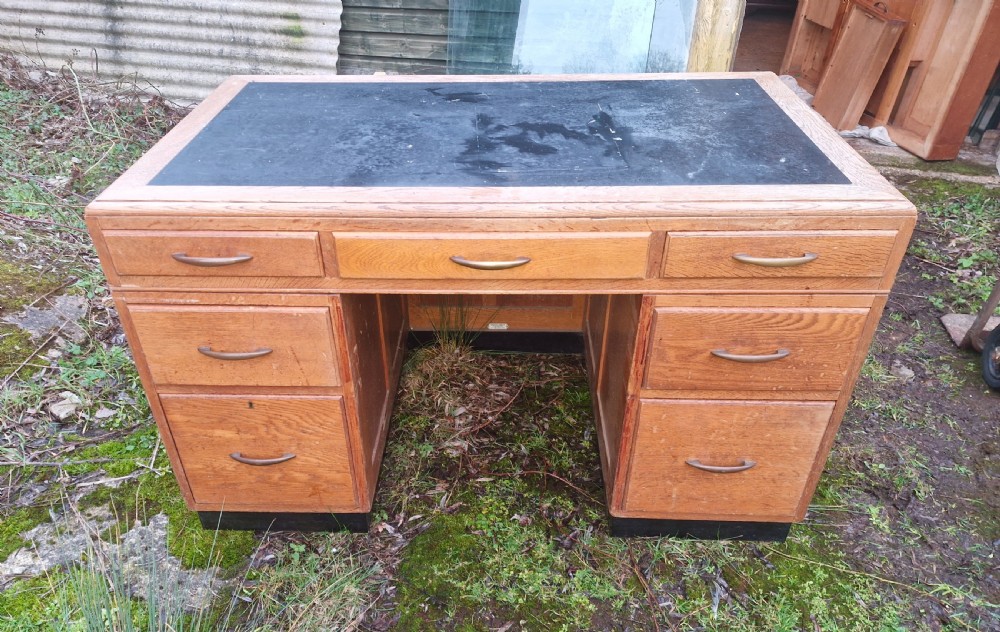 An Art Deco oak pedestal office desk featuring a dark inset writing top, streamlined drawers, and metal pull handles. View IV