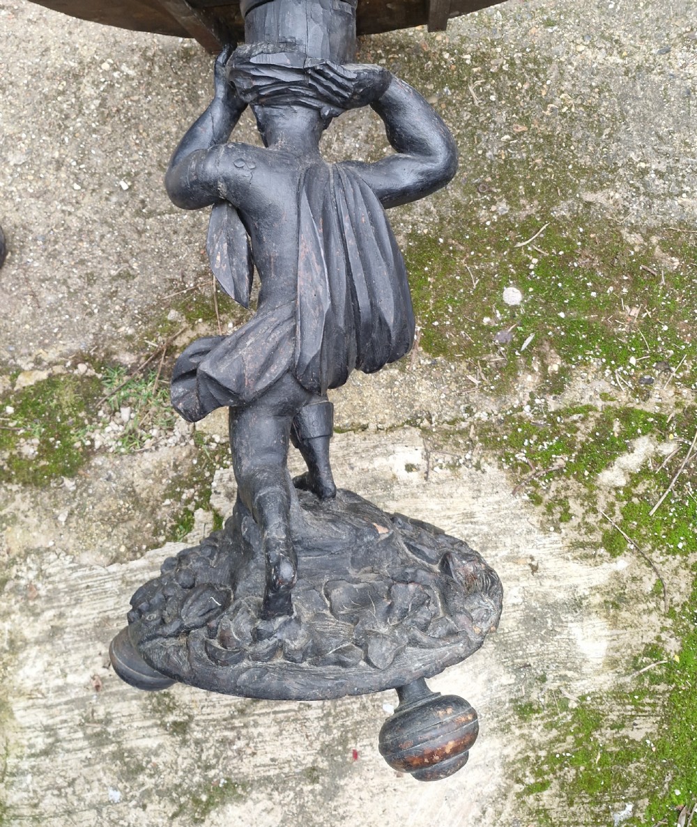 A carved ebonised wooden occasional table featuring a figural pedestal base supporting a circular top with a leaf-carved border. View VI