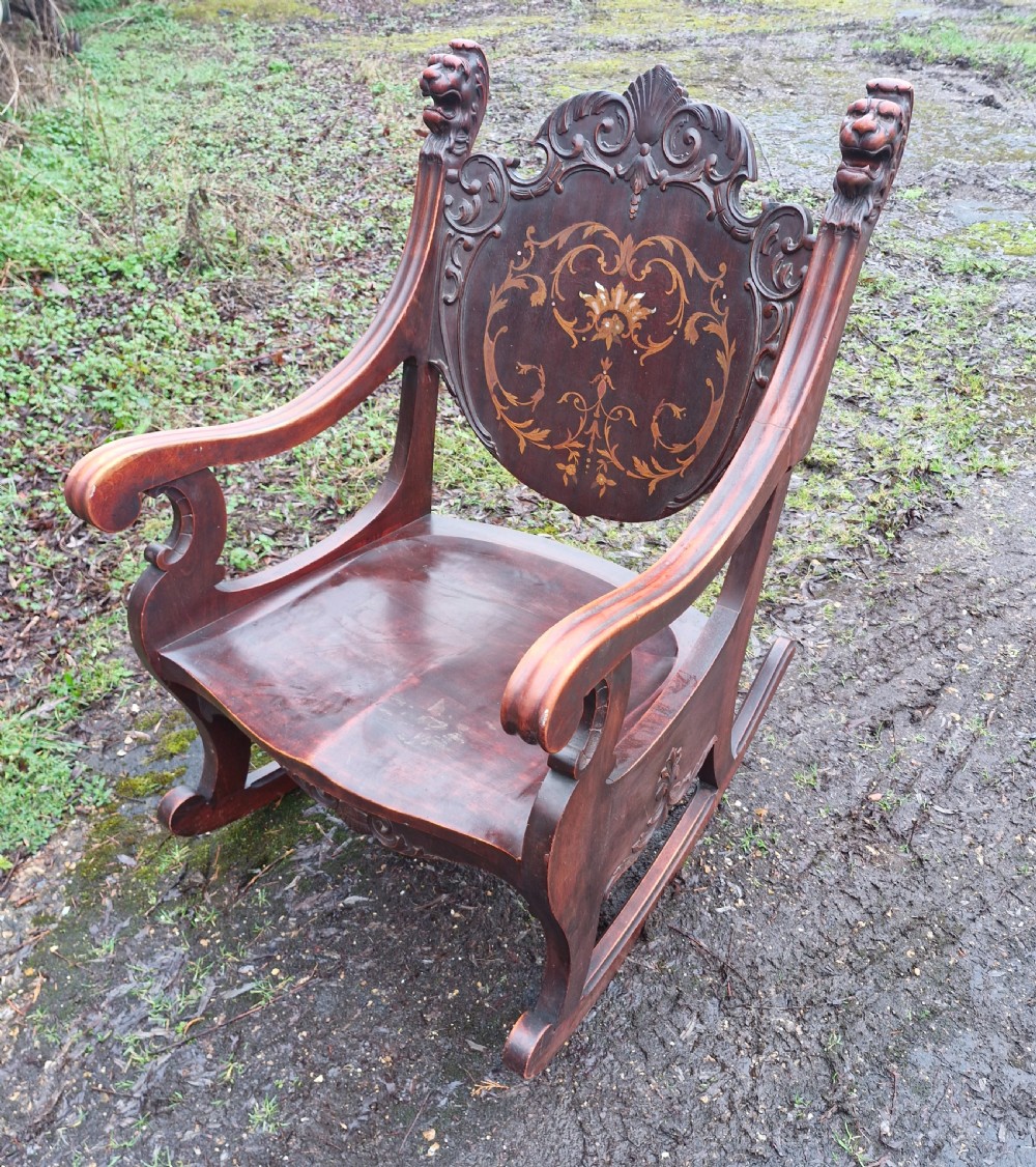 A late 19th-century dark mahogany rocking armchair featuring carved lion head uprights and a floral inlaid backrest.