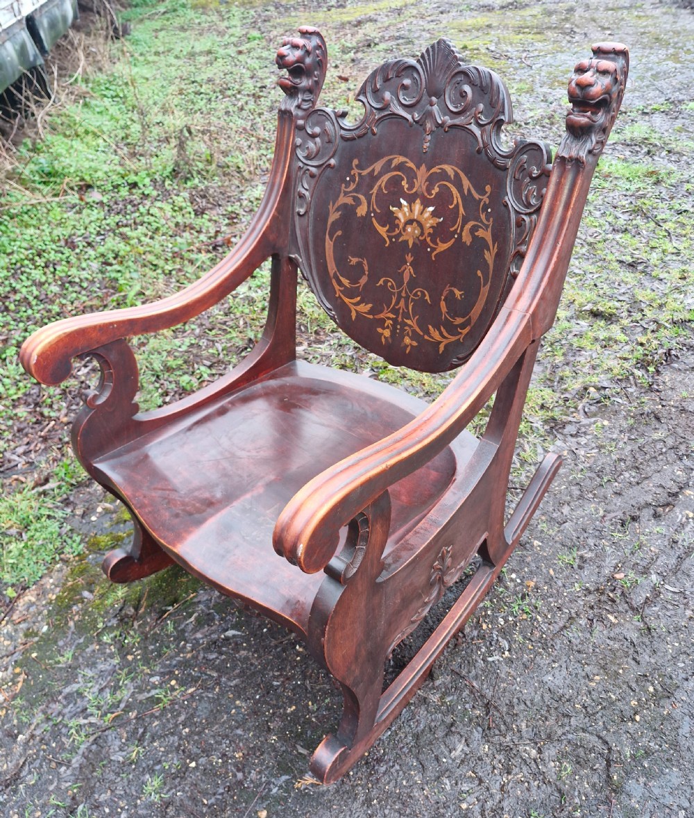 A late 19th-century dark mahogany rocking armchair featuring carved lion head uprights and a floral inlaid backrest. View II
