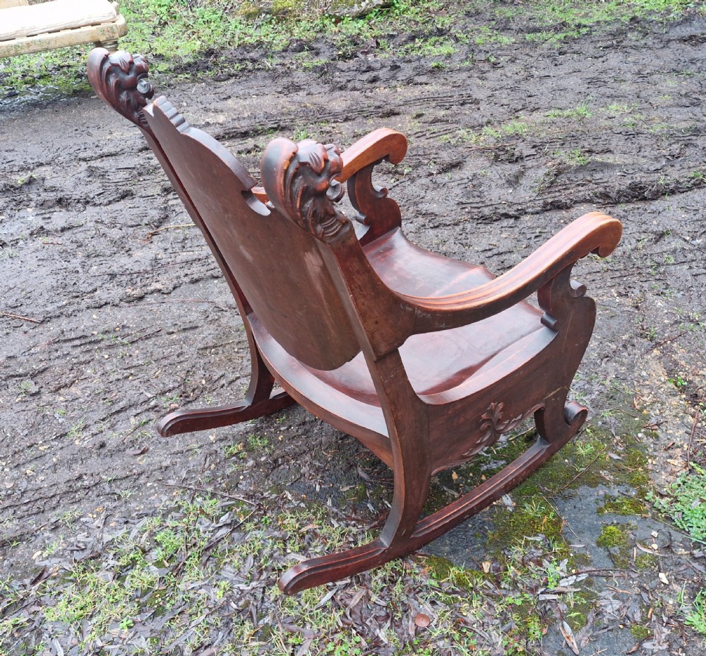 A late 19th-century dark mahogany rocking armchair featuring carved lion head uprights and a floral inlaid backrest. View III