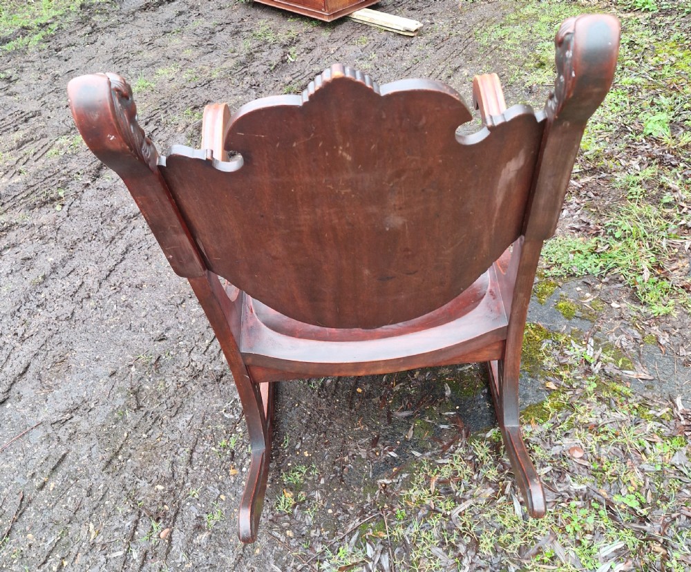 A late 19th-century dark mahogany rocking armchair featuring carved lion head uprights and a floral inlaid backrest. View IV