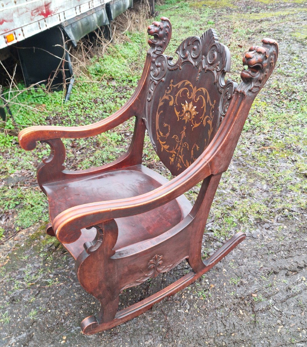 A late 19th-century dark mahogany rocking armchair featuring carved lion head uprights and a floral inlaid backrest. View VII