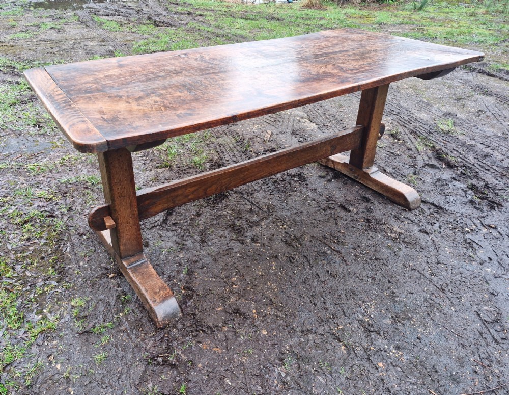 A rectangular solid oak refectory dining table with a thick plank top and trestle stretcher base.