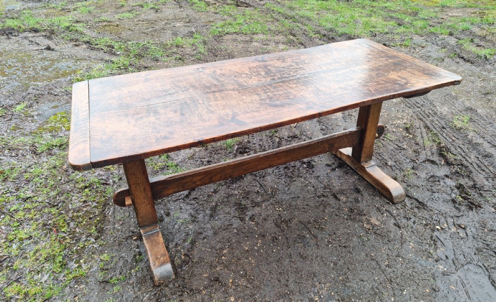 A rectangular solid oak refectory dining table with a thick plank top and trestle stretcher base. View VII
