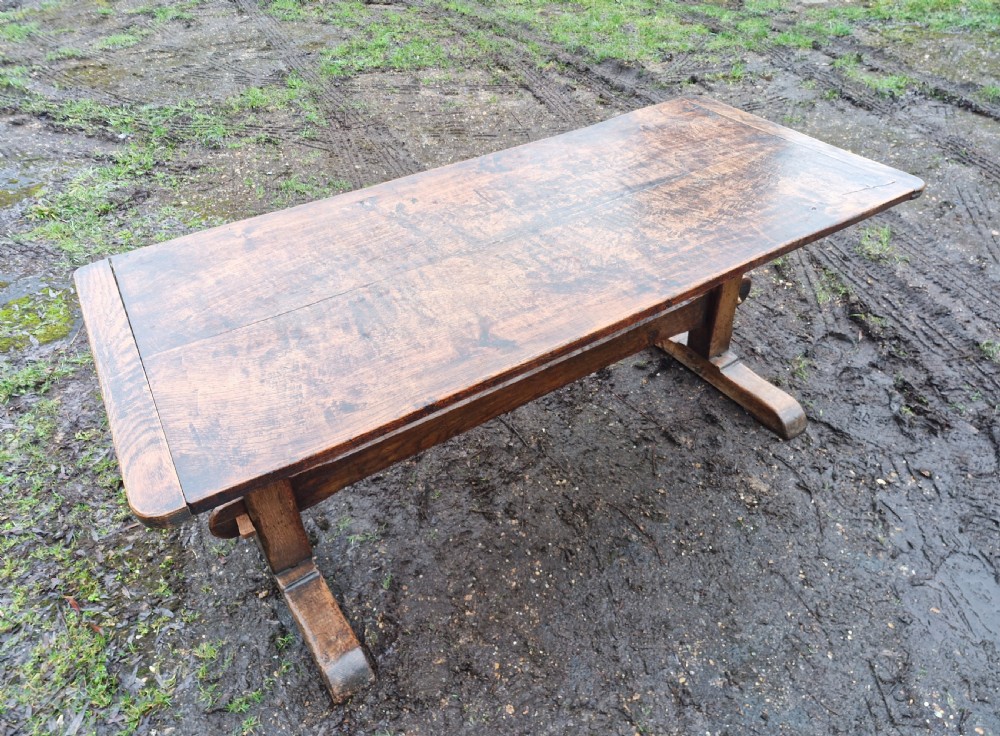 A rectangular solid oak refectory dining table with a thick plank top and trestle stretcher base. View VIII