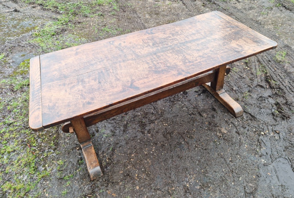 A rectangular solid oak refectory dining table with a thick plank top and trestle stretcher base. View IX