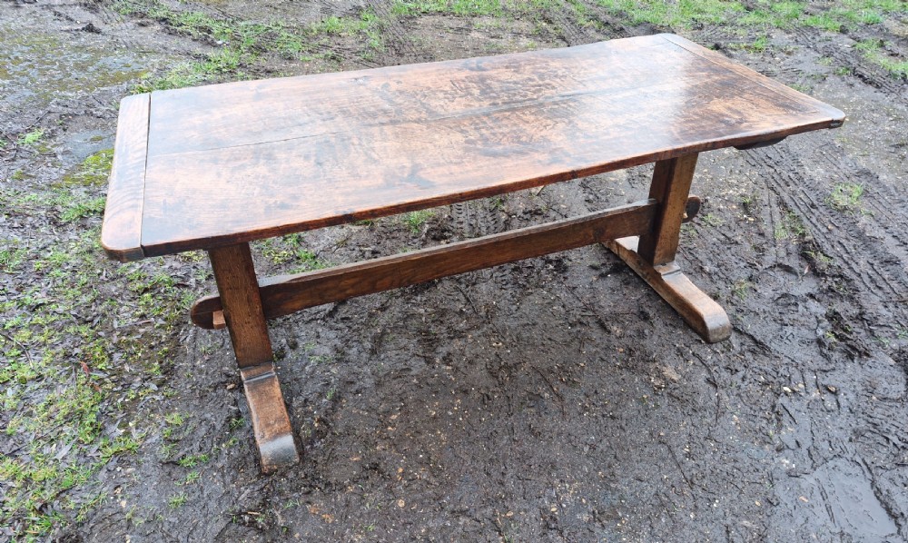 A rectangular solid oak refectory dining table with a thick plank top and trestle stretcher base. View X