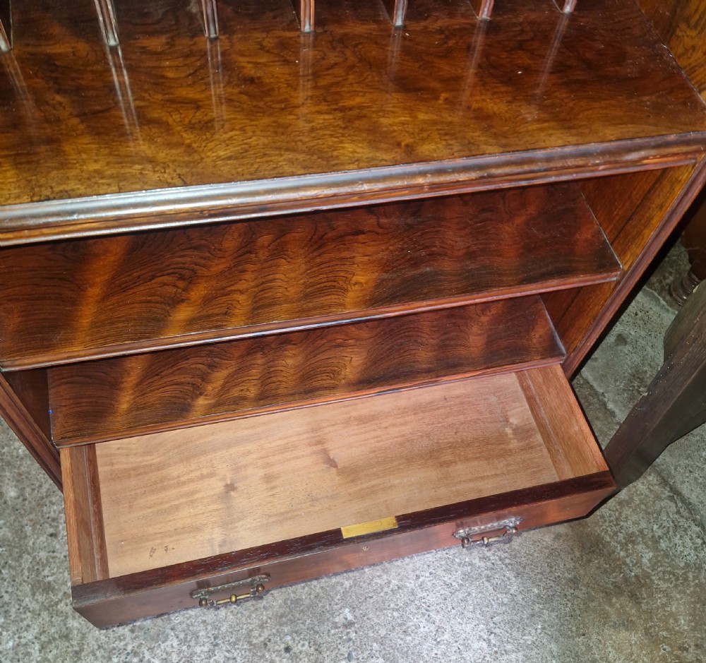A late Victorian dark rosewood side cabinet featuring upper tiered display shelves, vertical open folio partitions, lower open shelving, and small drawers with brass drop handles. View III