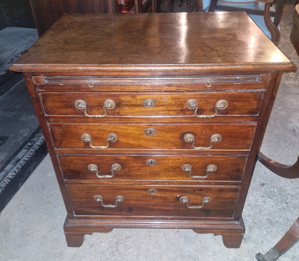 A compact Georgian mahogany chest of four drawers featuring a pull-out brushing slide, brass swan-neck handles, keyholes, and bracket feet.