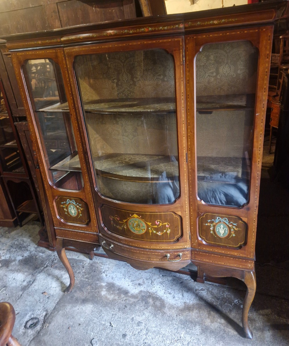 An Edwardian mahogany display cabinet with three glazed doors, hand-painted classical urn motifs, satinwood inlay, and cabriole legs.