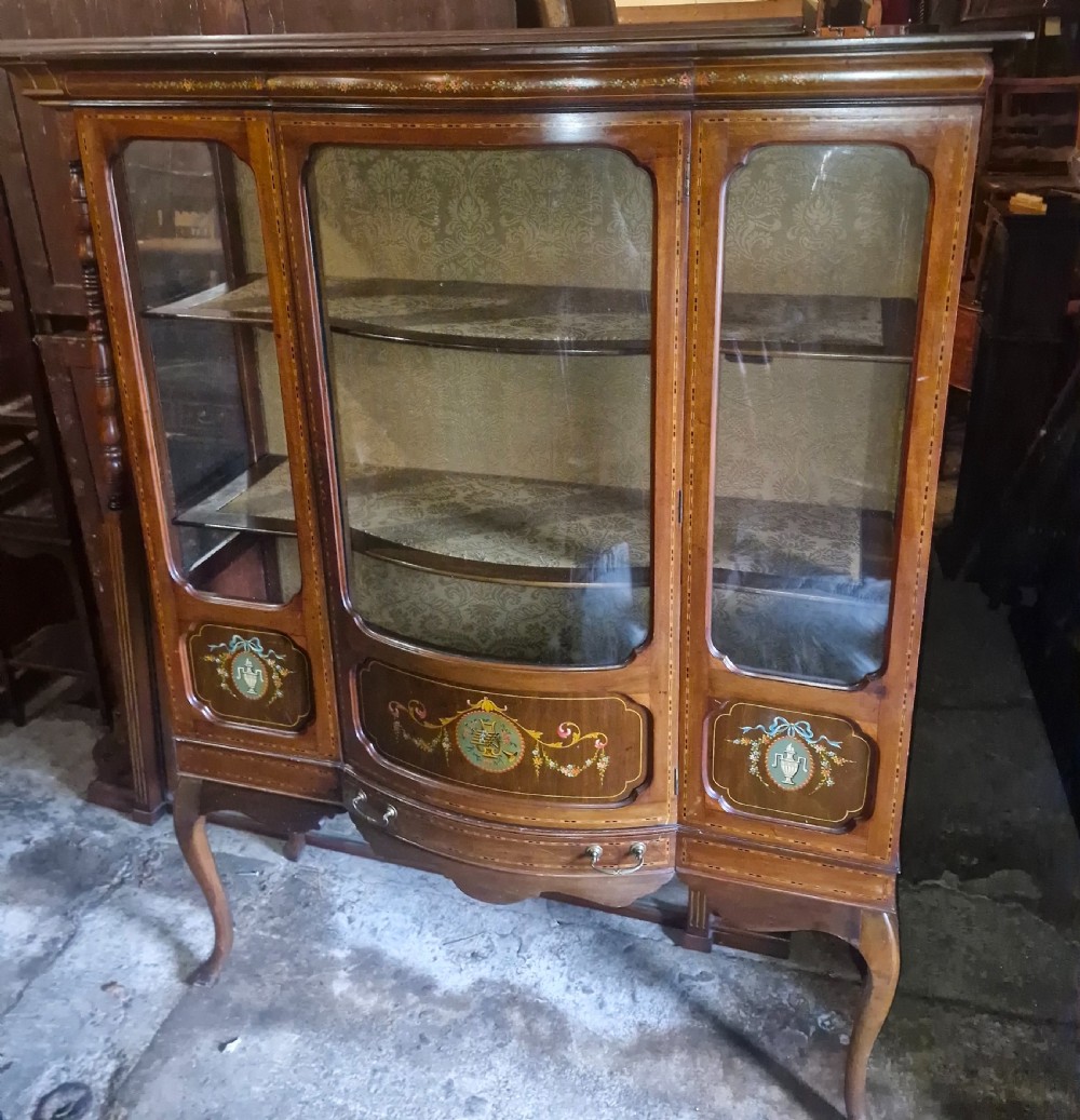 An Edwardian mahogany display cabinet with three glazed doors, hand-painted classical urn motifs, satinwood inlay, and cabriole legs. View II