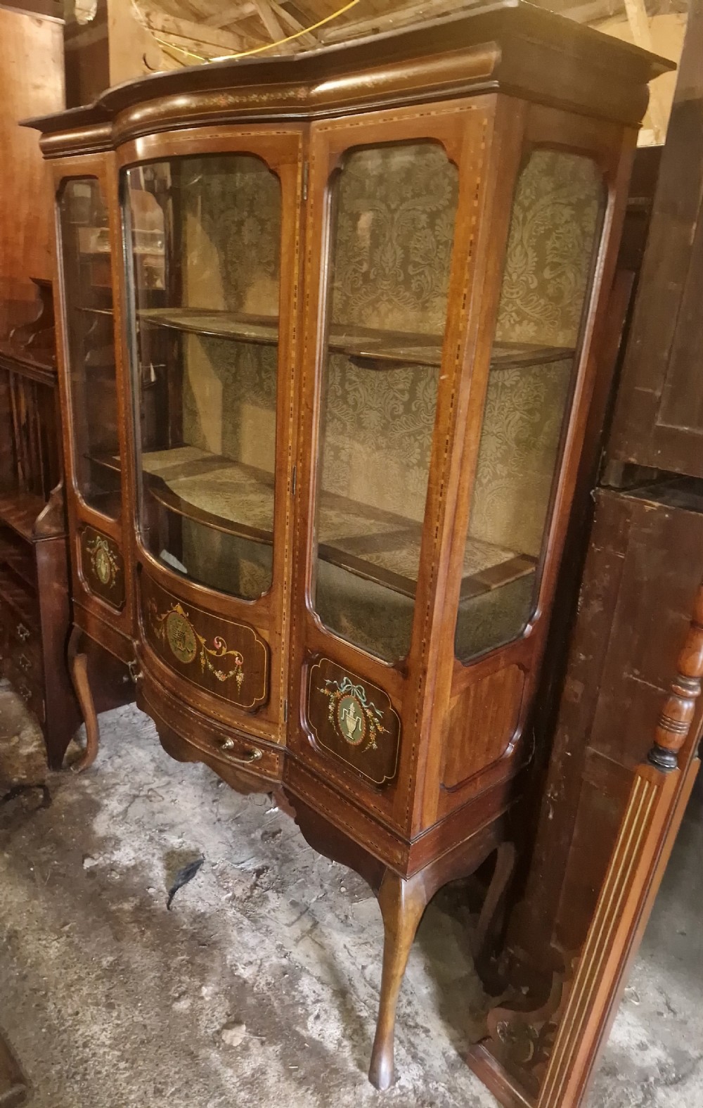 An Edwardian mahogany display cabinet with three glazed doors, hand-painted classical urn motifs, satinwood inlay, and cabriole legs. View V