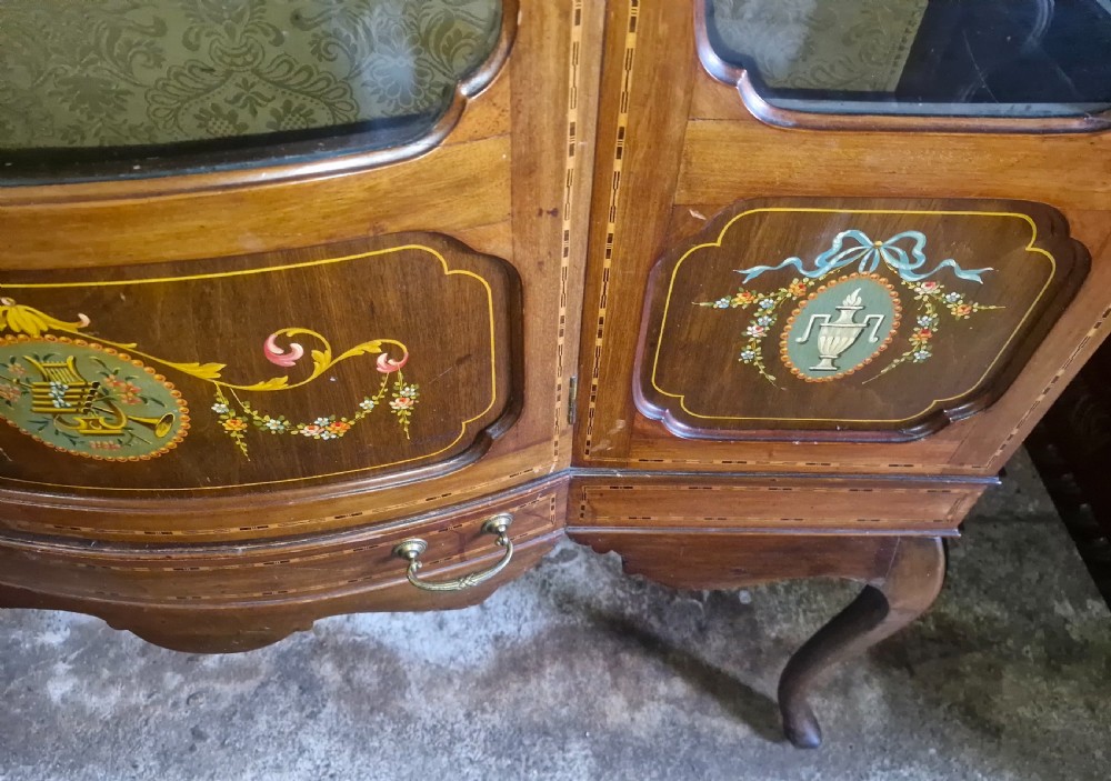 An Edwardian mahogany display cabinet with three glazed doors, hand-painted classical urn motifs, satinwood inlay, and cabriole legs. View VII
