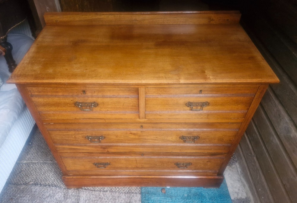 A late Victorian warm brown walnut chest of drawers featuring two short drawers over two long drawers with brass drop handles and a low top gallery.