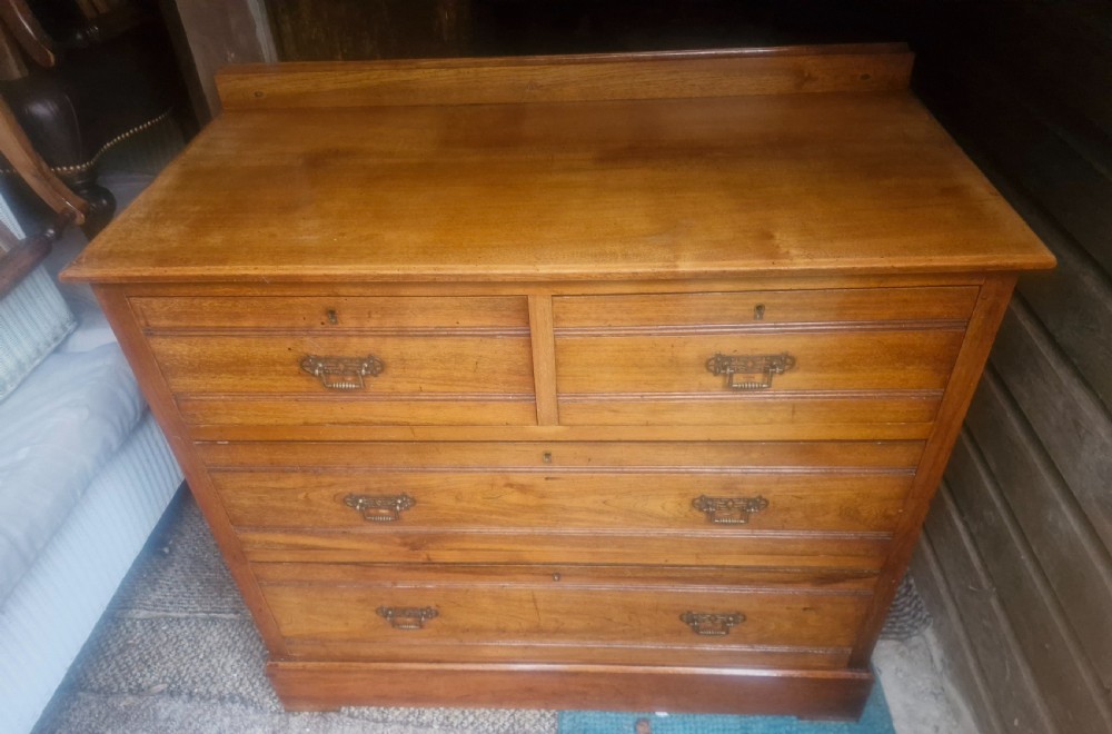 A late Victorian warm brown walnut chest of drawers featuring two short drawers over two long drawers with brass drop handles and a low top gallery. View IV