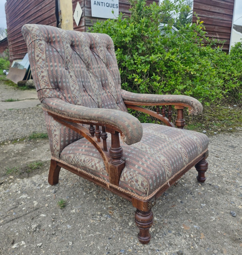 A late Victorian armchair featuring deep button-tufted fabric upholstery, turned front legs, and padded armrests supported by small turned wooden spindles.
