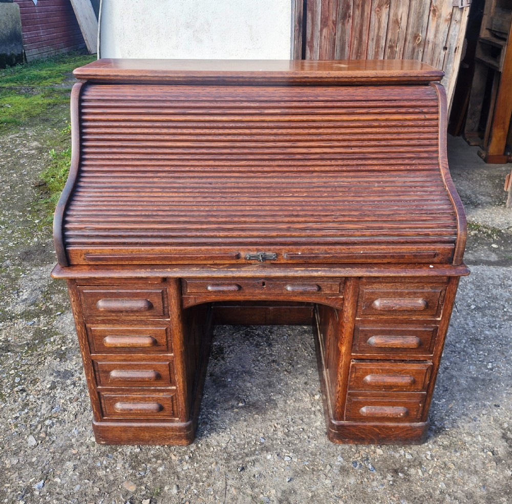 A traditional solid oak pedestal desk with a curved roll top tambour front and multiple side drawers.