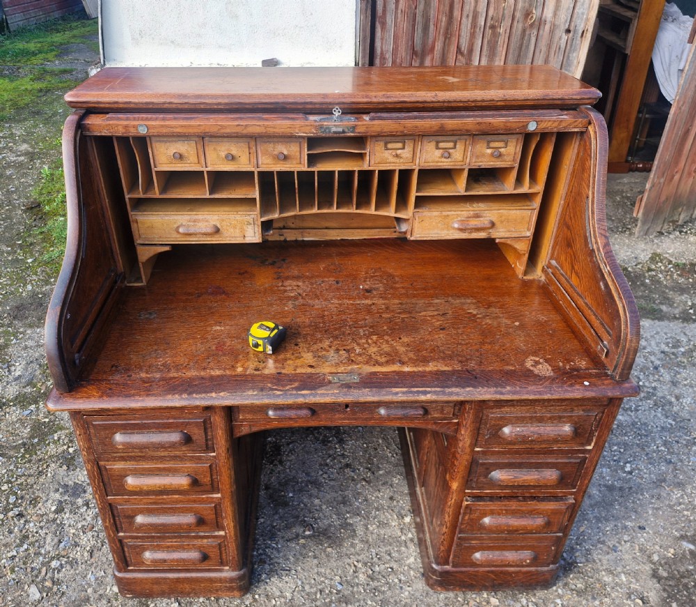 A traditional solid oak pedestal desk with a curved roll top tambour front and multiple side drawers. View III