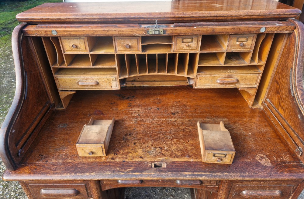 A traditional solid oak pedestal desk with a curved roll top tambour front and multiple side drawers. View IV