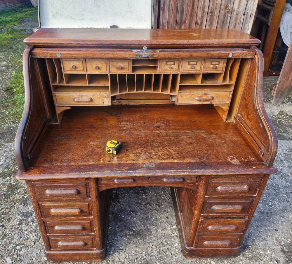 A traditional solid oak pedestal desk with a curved roll top tambour front and multiple side drawers. View V