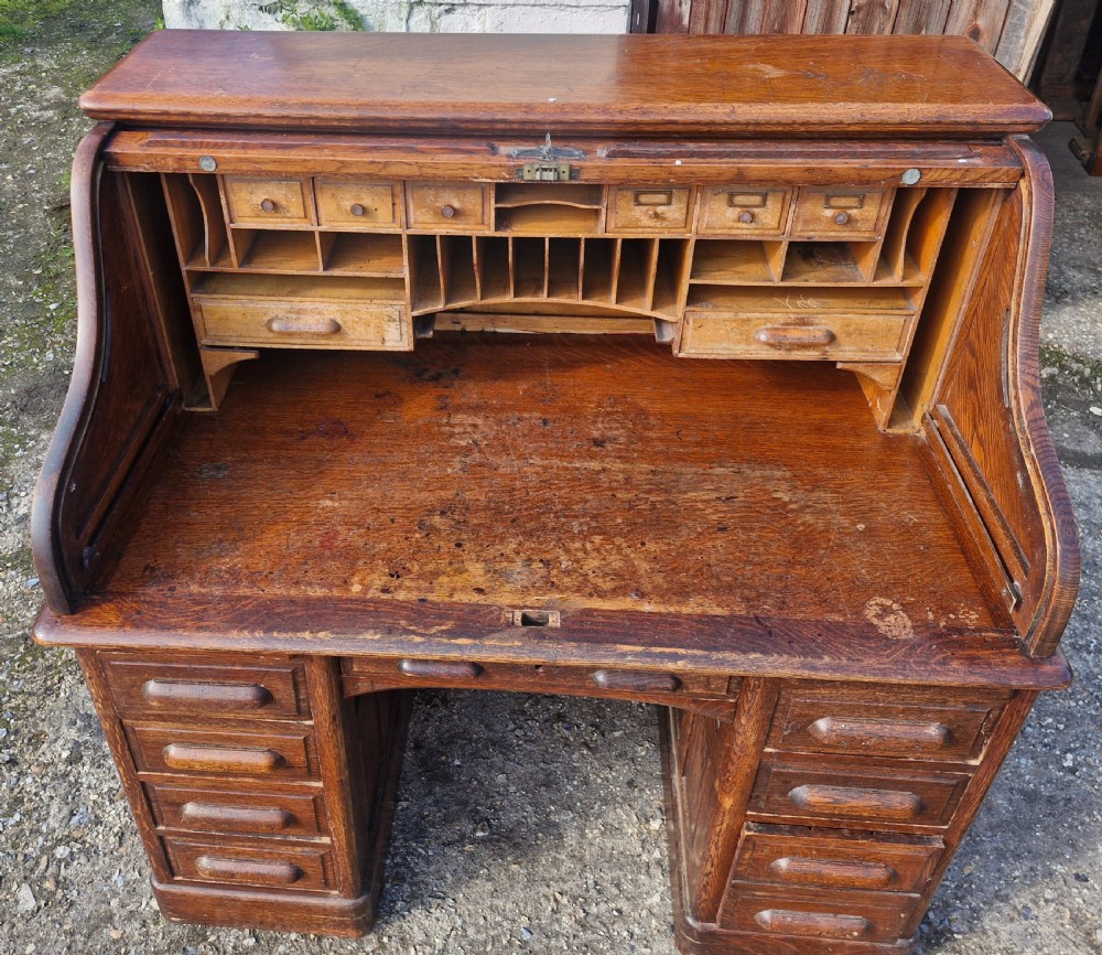 A traditional solid oak pedestal desk with a curved roll top tambour front and multiple side drawers. View VI