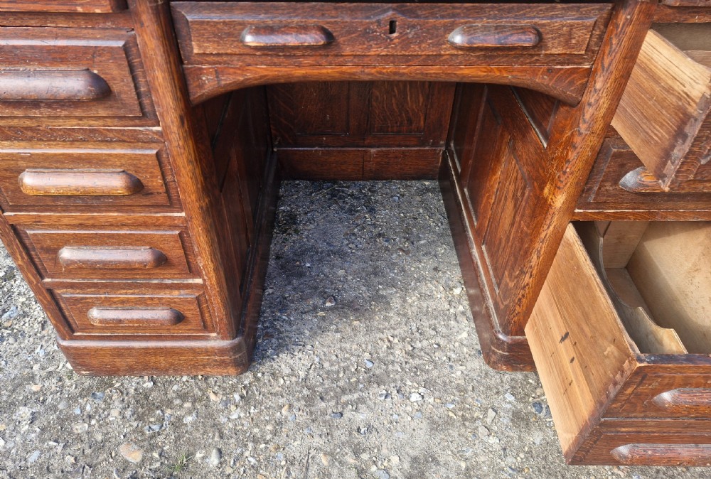 A traditional solid oak pedestal desk with a curved roll top tambour front and multiple side drawers. View VIII