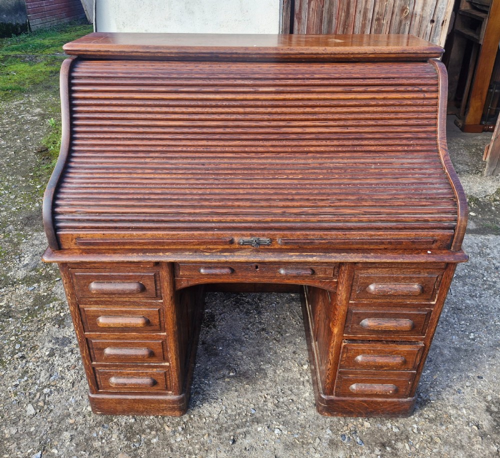 A traditional solid oak pedestal desk with a curved roll top tambour front and multiple side drawers. View IX
