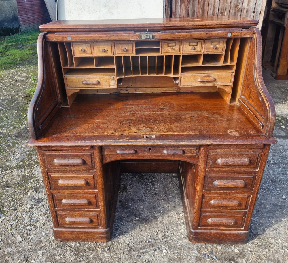 A traditional solid oak pedestal desk with a curved roll top tambour front and multiple side drawers. View XIII