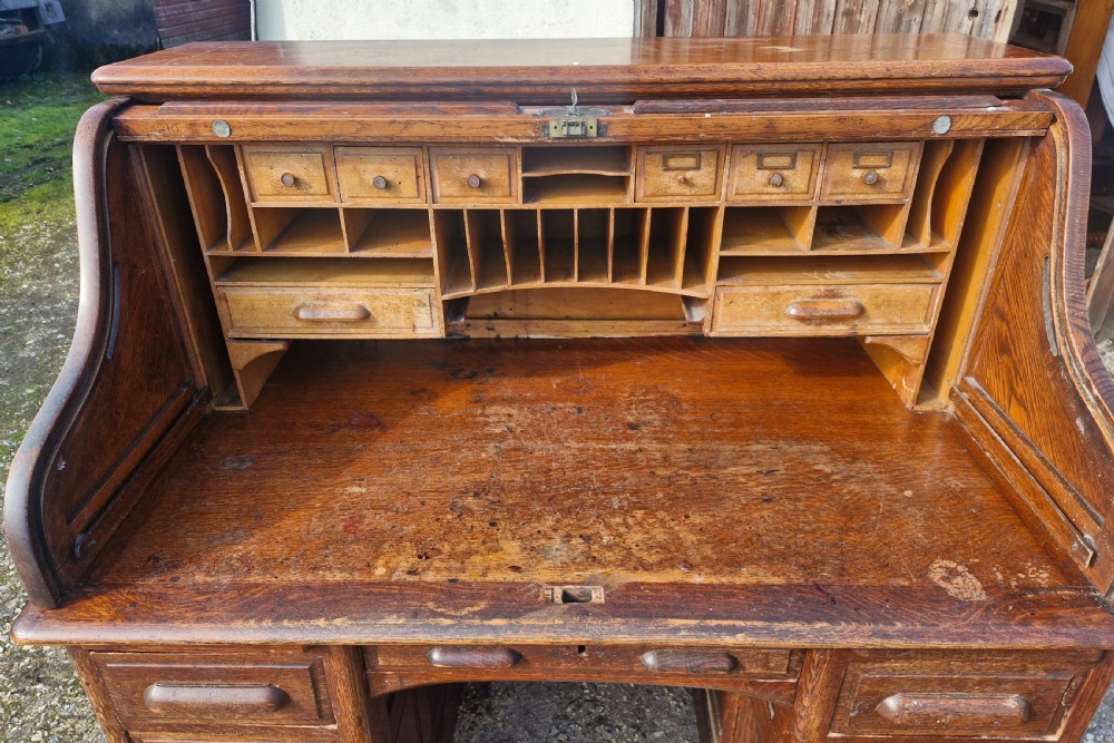 A traditional solid oak pedestal desk with a curved roll top tambour front and multiple side drawers. View XIV