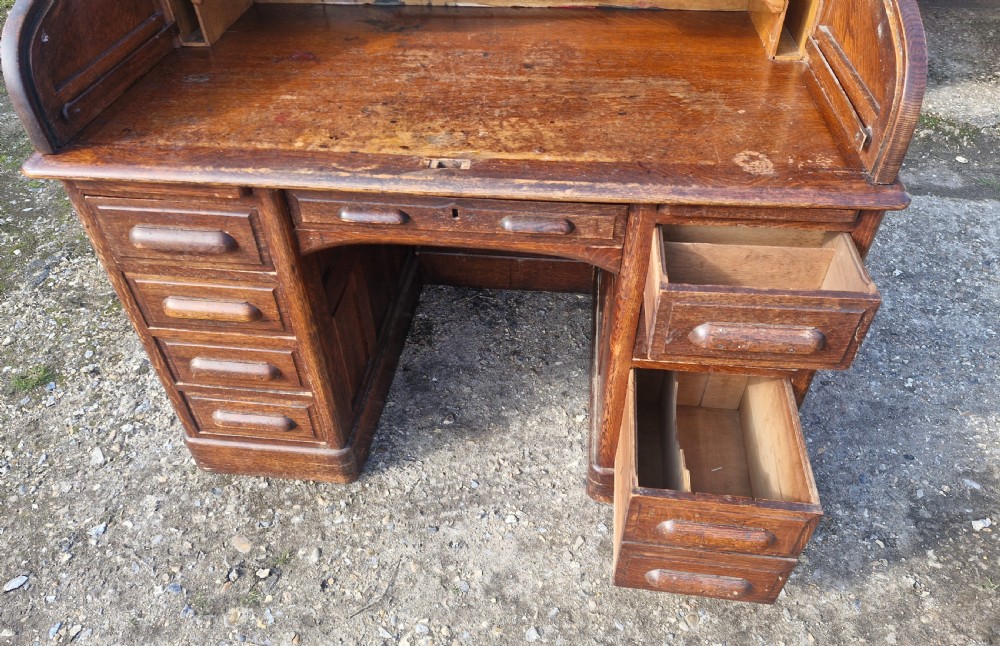 A traditional solid oak pedestal desk with a curved roll top tambour front and multiple side drawers. View XV