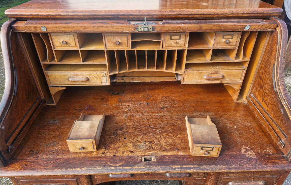 A traditional solid oak pedestal desk with a curved roll top tambour front and multiple side drawers. View XVIII