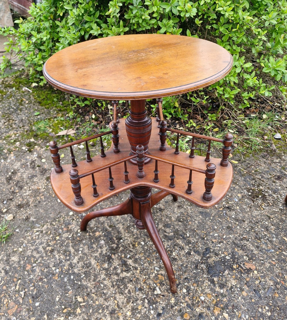 A Victorian mahogany revolving wine table featuring a circular top, a lower tier with spindle galleries, a turned central shaft, and three down-swept tripod legs.