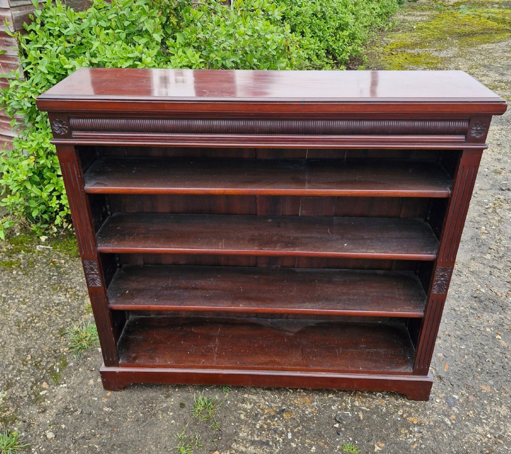 A low late Victorian mahogany open front bookcase featuring four tiers of shelving, reeded pilasters, and carved floral rosettes.