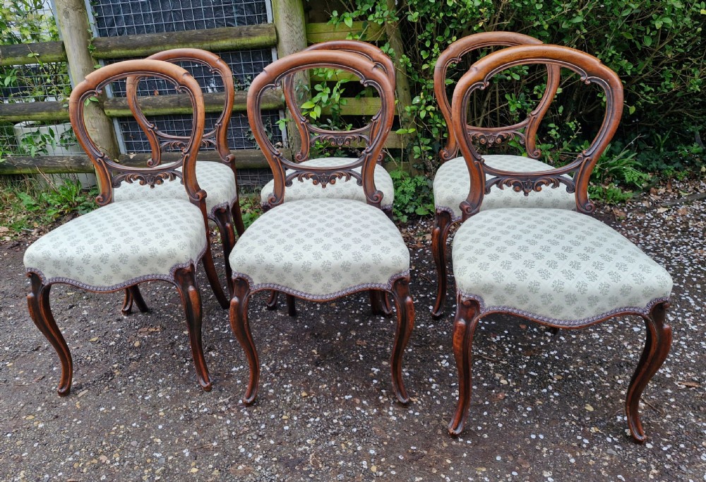 A set of six Victorian walnut balloon back dining chairs featuring carved back splats, cabriole front legs, and pattern-upholstered seats.