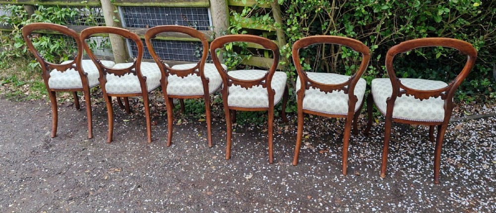 A set of six Victorian walnut balloon back dining chairs featuring carved back splats, cabriole front legs, and pattern-upholstered seats. View V