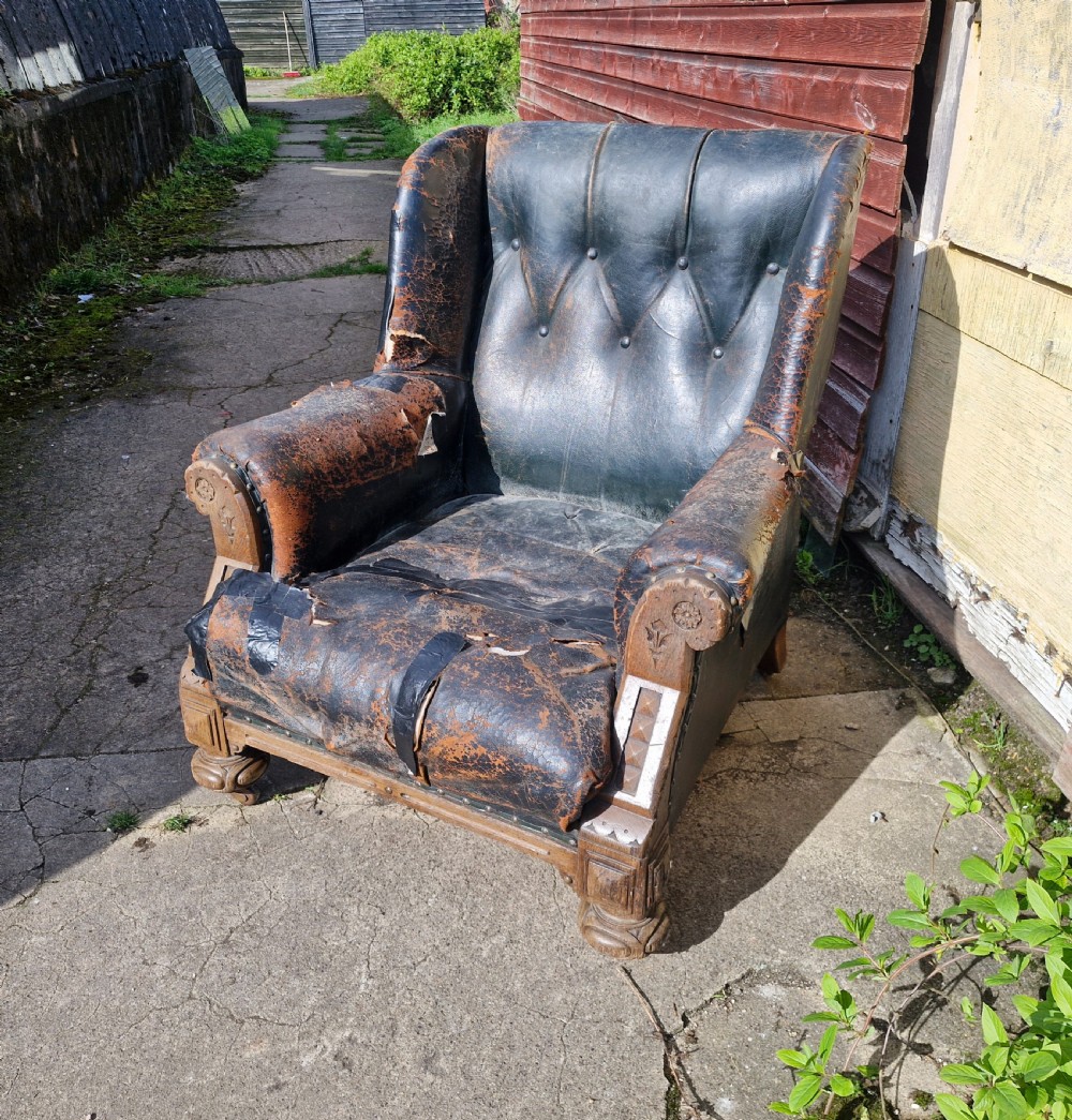 A Victorian library armchair featuring deep buttoned dark leather upholstery with carved wooden arm supports and feet.