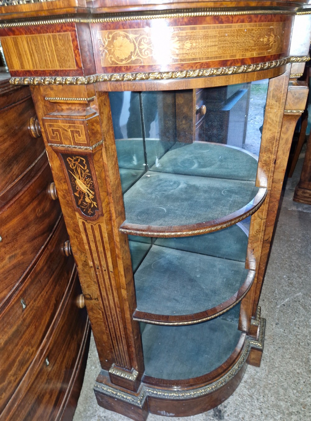 An antique burr walnut side cabinet featuring intricate marquetry inlays, gilt bronze mounts, a central mirror, and open curved side shelves lined in green velvet. View IV